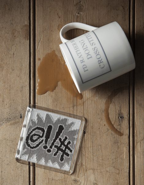 Coffee spill on wooden surface with a cross-stitch kit and mug, illustrating common cross-stitch mis.