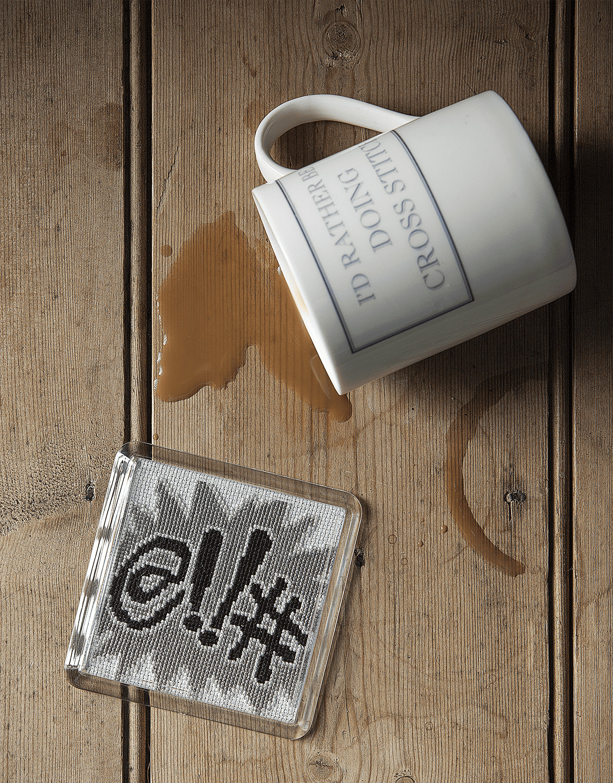 Coffee spill on wooden surface with a cross-stitch kit and mug, illustrating common cross-stitch mis.