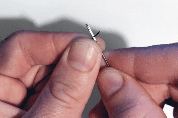 A short wet thread should be sufficiently stiff for you to guide the needle onto it