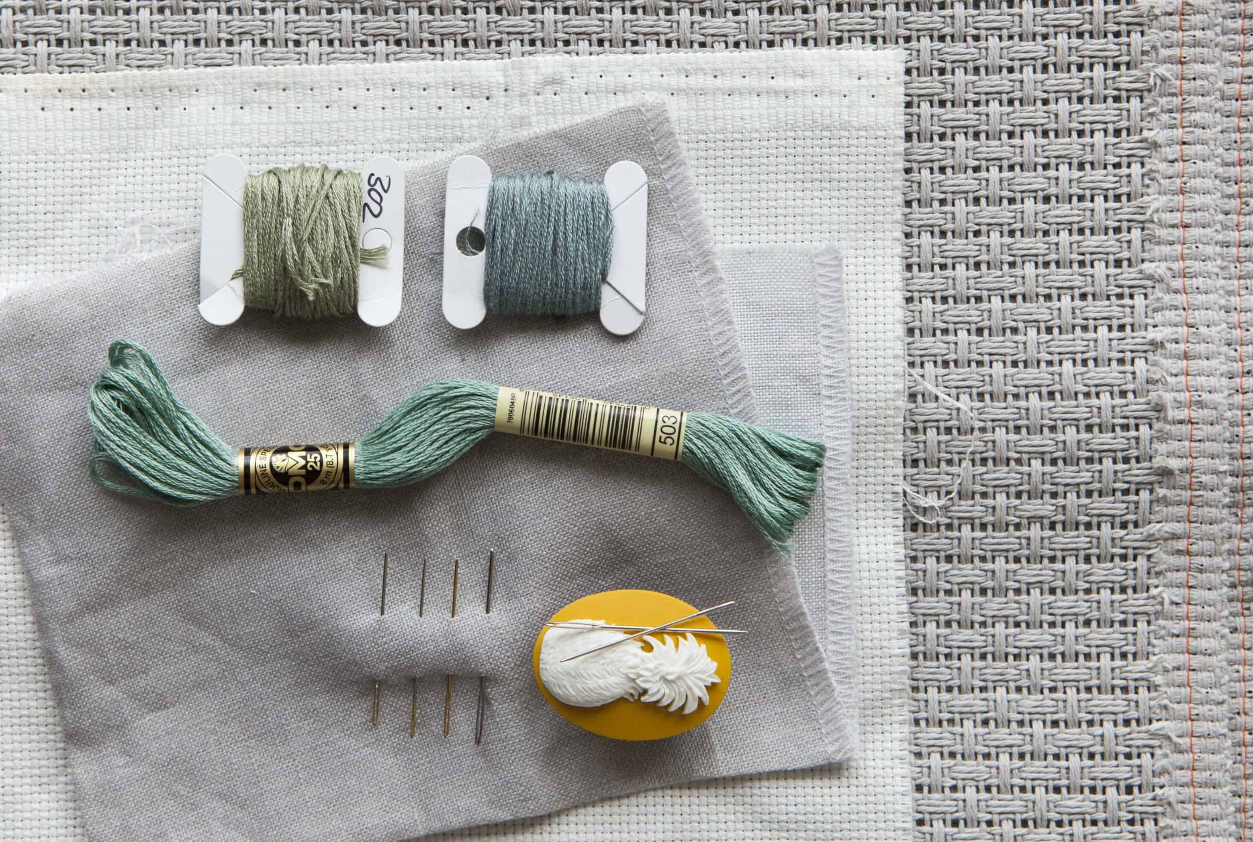 A colourful collection of embroidery threads, needles, and fabric for cross-stitch projects.