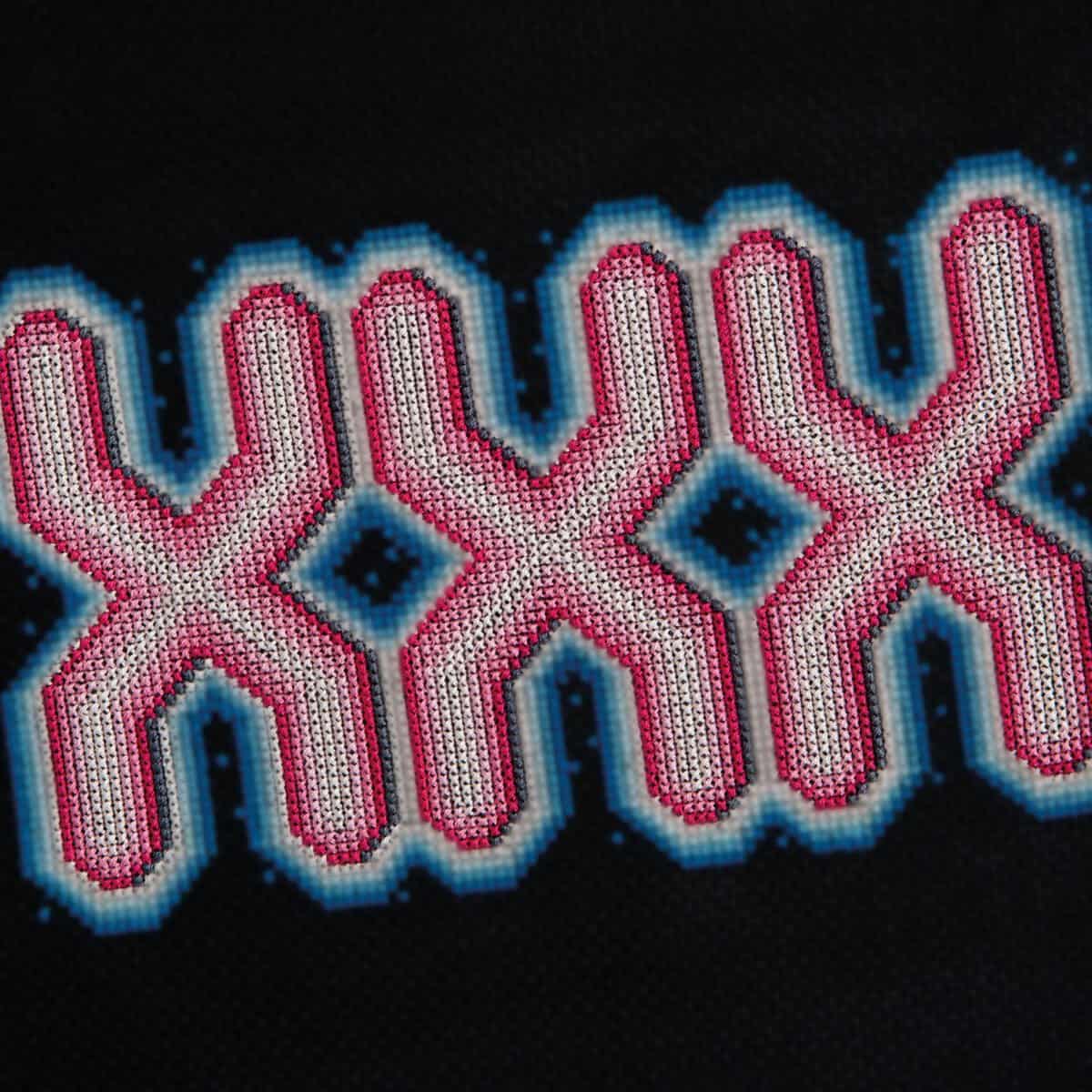 Beaded geometric cross-stitch pattern with pink, blue, and black colours on black fabric.